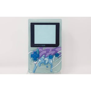 Op de afbeelding: Een doorzichtige blauwe Game Boy Color met een paars en blauw Suicune Pokemon-ontwerp. Het scherm is zwart-wit en de tekst "GAME BOY COLOR" is zichtbaar op de voorkant van het apparaat.
