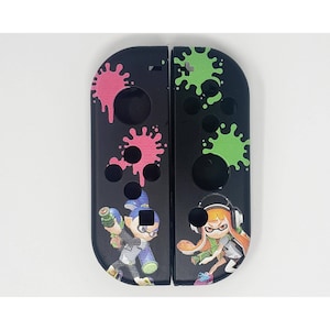 May include: A black Nintendo Switch Joy-Con controller shell with a Splatoon 2 design. The shell features green and pink paint splatters, and characters from the game, including a squid and an octopus.