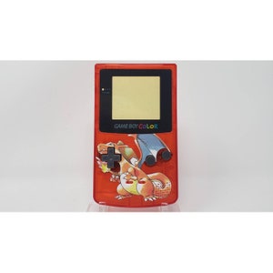 Puede incluir: Una consola de videojuegos portátil Game Boy Color roja con un diseño de personaje Charizard. La consola tiene una pantalla negra y botones negros.