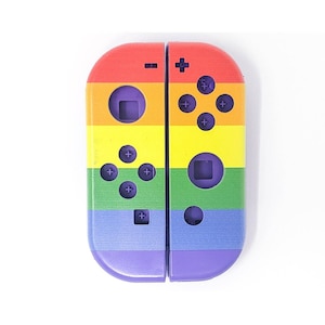 Puede incluir: Una carcasa de Joy-Con de Nintendo Switch de colores arcoíris con detalles en morado. La carcasa tiene un diseño de rayas arcoíris con rayas rojas, naranjas, amarillas, verdes, azules y moradas.