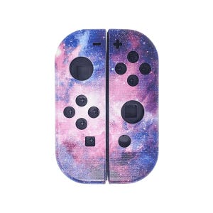 May include: A pair of galaxy-themed Nintendo Switch Joy-Con controllers. The controllers are a light pink and blue with a galaxy print. The controllers have black buttons and a black Nintendo logo.