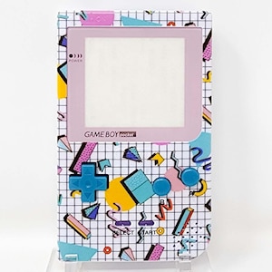 May include: A white Game Boy Pocket handheld video game console with a pink and blue geometric pattern. The console has a white screen with a pink border and the text "GAME BOY pocket" printed on the front.