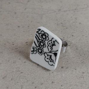 Peut inclure: Bague blanche avec un motif floral noir. La bague est en céramique et possède une bande argentée.