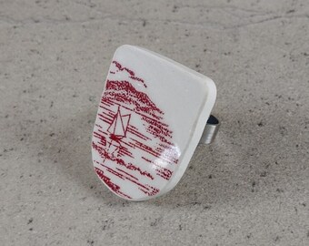 May include: A white ceramic ring with a red and white design of a sailboat on a body of water. The ring is attached to a silver band.