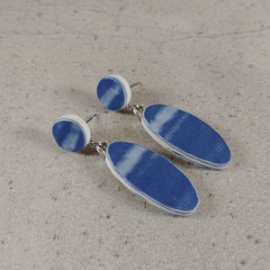 Puede incluir: Un par de pendientes ovalados de color azul y blanco con un círculo blanco en la parte superior de cada pendiente.