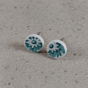 Puede incluir: Un par de pequeños pendientes redondos con fondo blanco y diseño floral verde.