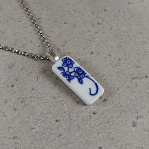 May include: A silver chain necklace with a rectangular pendant featuring a blue and white floral design. The pendant is made from a piece of vintage china.