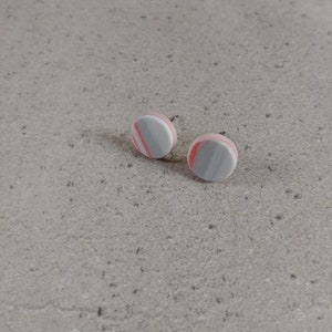 Może przedstawiać: Para małych, okrągłych kolczyków z biało-szaro-różowym wzorem w paski.