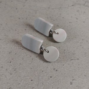 Peut inclure: Une paire de boucles d'oreilles pendantes à rayures grises et blanches avec un pendentif rond blanc. Les boucles d'oreilles ont un crochet argenté.