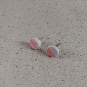May include: A pair of small, round stud earrings with a pink and gray color scheme. The earrings are made of polymer clay and have a simple, modern design.