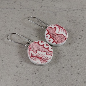 May include: A pair of red and white dangle earrings with a floral pattern. The earrings have silver hooks.