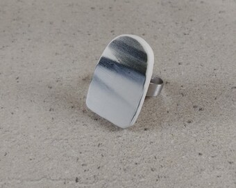 May include: A white and black marbled ring with a silver band. The ring is made of polymer clay and is a unique statement piece.