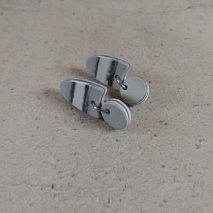 Peut inclure: Une paire de boucles d'oreilles en céramique blanche avec des rayures bleues et grises. Les boucles d'oreilles ont la forme d'une larme et sont munies d'un petit anneau argenté en haut.