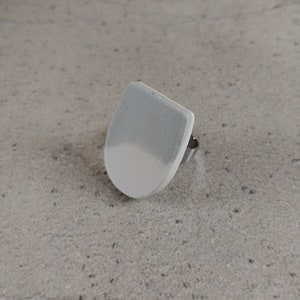 Könnte beinhalten: Ein weißer und grauer Keramikring mit einem silbernen Band. Der Ring ist schildförmig.