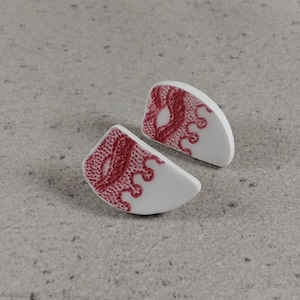 Könnte beinhalten: Ein Paar weiße Keramikohrringe mit rotem Spitzenmuster. Die Ohrringe sind halbkreisförmig.