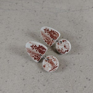 Peut inclure: Une paire de boucles d'oreilles pendantes avec une base blanche et un motif floral brun. Les boucles d'oreilles sont en pâte polymère et ont un connecteur métallique argenté.