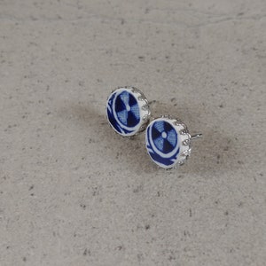 Könnte beinhalten: Ein Paar blaue und weiße Porzellanohrringe mit einem silberfarbenen Metallrand. Die Ohrringe haben ein kreisförmiges Design mit einem blauen und weißen Muster.