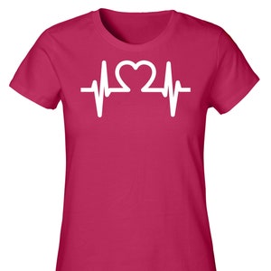 Könnte beinhalten: Ein pinkfarbenes T-Shirt mit einem weißen Herzschlag-Motiv. Das Motiv zeigt ein Herzsymbol in der Mitte der Herzschlaglinie.
