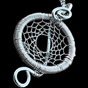 May include: A silver dreamcatcher pendant necklace with a circular wire frame and a delicate web design. The pendant is attached to a silver chain.