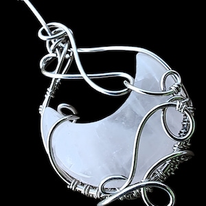 May include: A silver wire-wrapped pendant featuring a crescent-shaped clear quartz crystal.