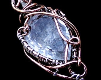 May include: A clear quartz crystal pendant wrapped in copper and silver wire. The pendant has a delicate, intricate design and hangs from a silver chain.