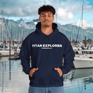 May include: A navy blue hooded sweatshirt with the text "TITAN EXPLORER PETERSBURG, AK" printed in white on the front.