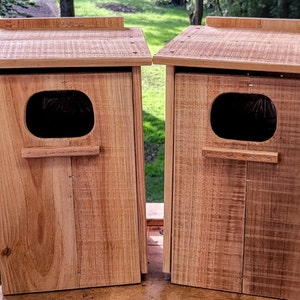 May include: Two wooden birdhouses with a small opening for birds to enter. The birdhouses are made of natural wood with a light brown color.