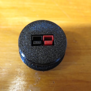 Puede incluir: Primer plano de una terminal de altavoz redonda negra con dos conectores de cable de altavoz rojo y negro.