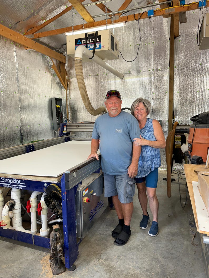 Bruce and Mary Amick standing beside a computerized numerical cutting machine that cuts our yard art signs