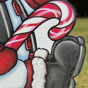 a Christmas snowman lawn sign: A red and white candy cane with a red and white striped pattern. The candy cane is wrapped around a white and blue object with a red trim. The object is covered in glitter.