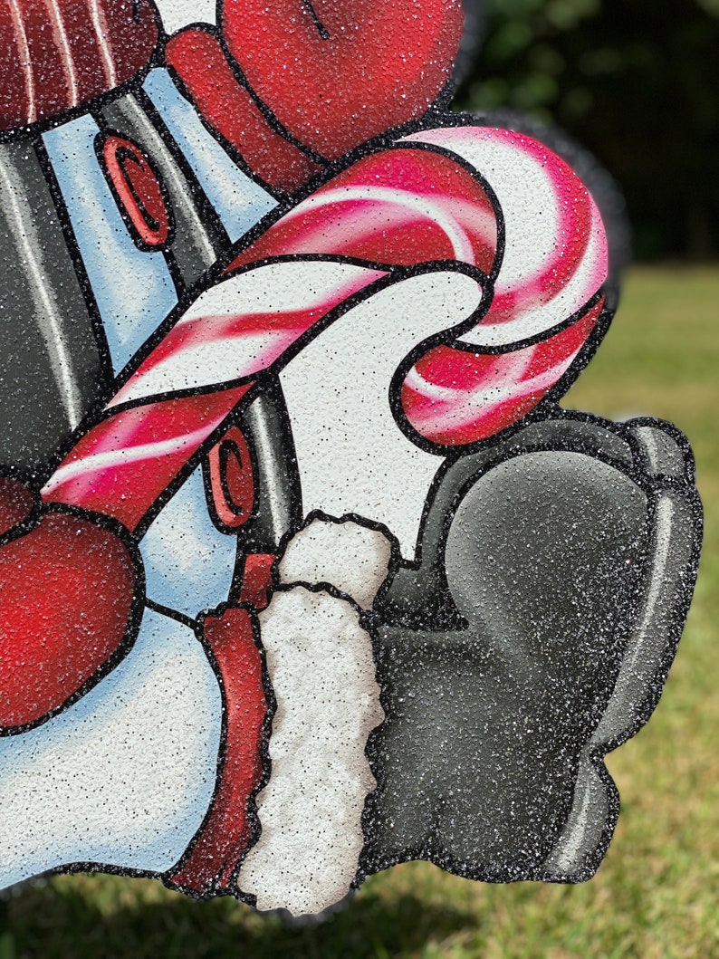 a Christmas snowman lawn sign: A red and white candy cane with a red and white striped pattern. The candy cane is wrapped around a white and blue object with a red trim. The object is covered in glitter.