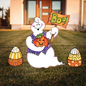 May include: A white ghost holding a jack-o-lantern pumpkin and a sign that says "Boo!" with two yellow and orange candy corn decorations on either side.