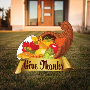 May include: A cornucopia filled with fall harvest fruits and vegetables, including corn, grapes, apples, and pumpkins. A gold ribbon with the text "Give Thanks" is displayed below the cornucopia.