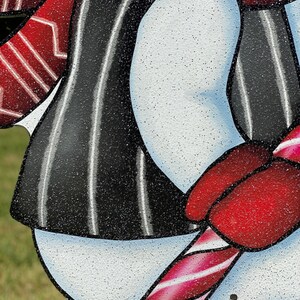 a Christmas snowman lawn sign: A snowman with a black and white striped shirt, a red hat, and a red and white candy cane in its hand.