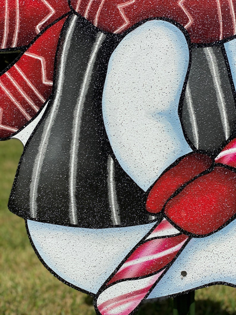 a Christmas snowman lawn sign: A snowman with a black and white striped shirt, a red hat, and a red and white candy cane in its hand.