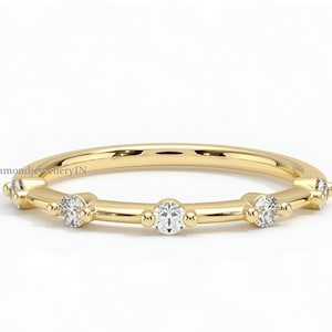 Op de afbeelding: Een delicate gouden ring met vijf kleine ronde diamanten die in een rij zijn gezet. De diamanten zijn bezel gezet en de band is glad en gepolijst.