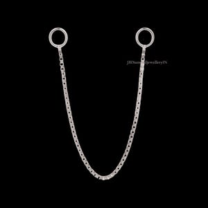 May include: A silver chain with two circular loops at the top, connected by a delicate chain. The chain hangs in a gentle curve against a black background. The jewelry piece is simple and elegant.