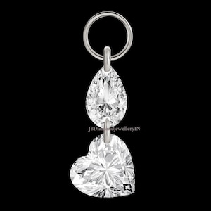 Pode incluir: Um pingente de prata com um diamante em forma de pêra e um diamante em forma de coração. Os diamantes são conectados por uma corrente de prata e suspensos de um anel de prata. O fundo é preto. O texto "JBDiamondJewelleryIN" é visível.