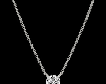 Puede incluir: Un collar de plata con un gran colgante de piedra preciosa clara y redonda. El colgante está engastado en un engaste simple de cuatro garras. La cadena es delicada y está hecha de pequeñas piezas de plata unidas. El fondo es negro.