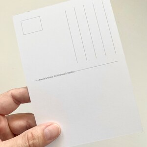 May include: A white postcard with vertical lines for writing and a small rectangle for a stamp. The text "Sonne & Mond" &copy; 2023 una.kritzolina is printed at the bottom. The postcard is held in a hand.