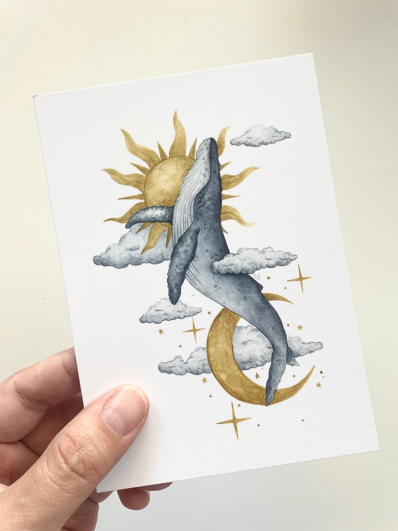 May include: Watercolor art print featuring a whale leaping towards a golden sun and moon. The artwork includes fluffy clouds and gold stars against a white background. The whale is depicted in shades of blue and gray.
