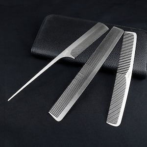 Könnte beinhalten: Ein Set aus drei silbernen Metallkämmen mit feinen Zähnen, angeordnet auf einem schwarzen Lederetui. Ein Kamm hat ein spitzes Ende, die anderen sind rechteckig. Das Wort "Jane" ist auf einem Kamm eingraviert, und "Tarvi" auf einem anderen.