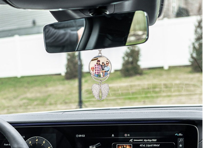 May include: A silver car charm with a round photo frame and angel wings. The photo frame has a picture of a family of three.