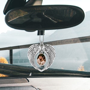 May include: Silver car charm with a heart-shaped frame and angel wings. A photo of a couple is visible in the frame.