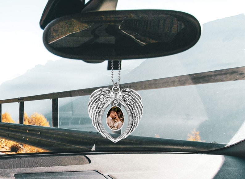 May include: Silver car charm with a heart-shaped frame and angel wings. A photo of a couple is visible in the frame.