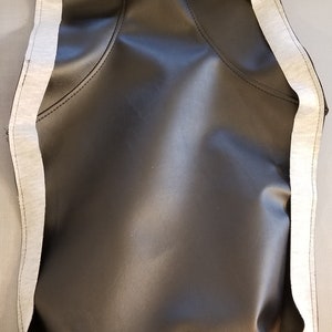 May include: A black leather item with a white border. The item has a curved shape with stitched seams and a smooth, shiny surface. The white border is made of a soft, textured material.