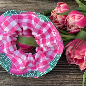 Könnte beinhalten: Ein Haargummi aus Stoff mit einem leuchtend pink-weißen Vichy-Karo-Muster auf der Innenseite und einem grünen Stoff mit kleinen weißen Punkten und pinken Blumenakzenten am äußeren Rand, präsentiert neben einem Strauß aus pinken und weißen Tulpen.