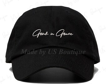 Puede incluir: Una gorra de béisbol negra con una inscripción bordada en blanco que dice "Grow in Grace". La gorra tiene una visera curvada y una correa en la parte posterior para ajustar el ajuste.