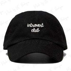 May include: A black baseball cap with white embroidered text that reads "introvert club".