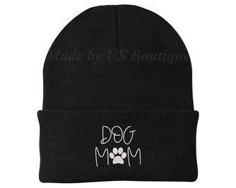May include: Black knit beanie with the words "DOG MOM" in white script and a white paw print. The text "Made by US Boutique" is printed in light gray across the top of the beanie.